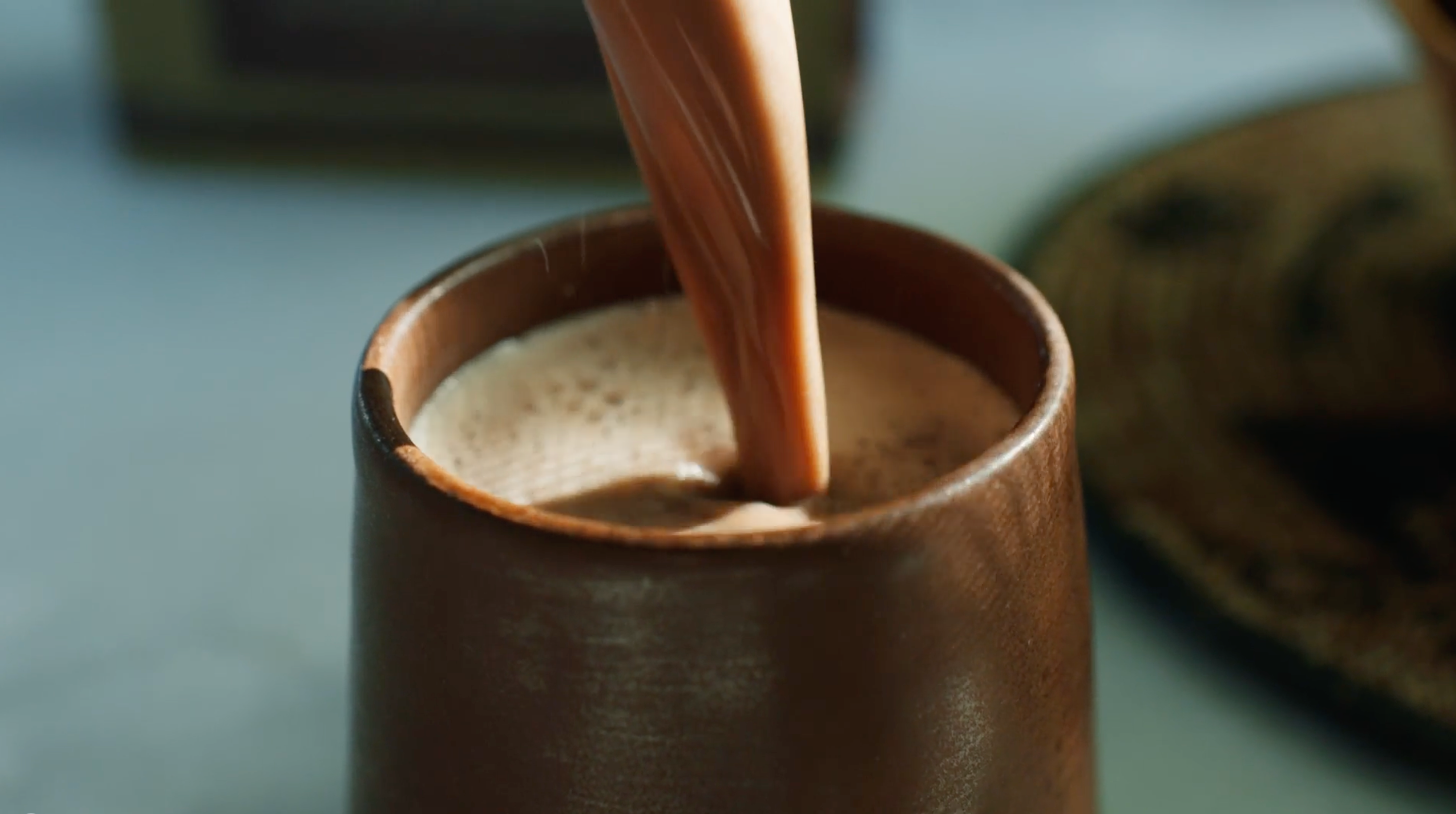 Cocoa being poured into a ceramic mug on a blurred background