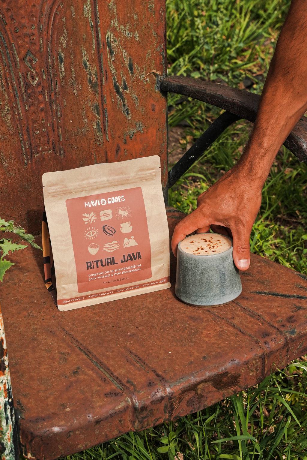 Hand reaching for a cup of coffee next to a package labeled 'Ritual Java' on a rustic wooden surface outdoors.

