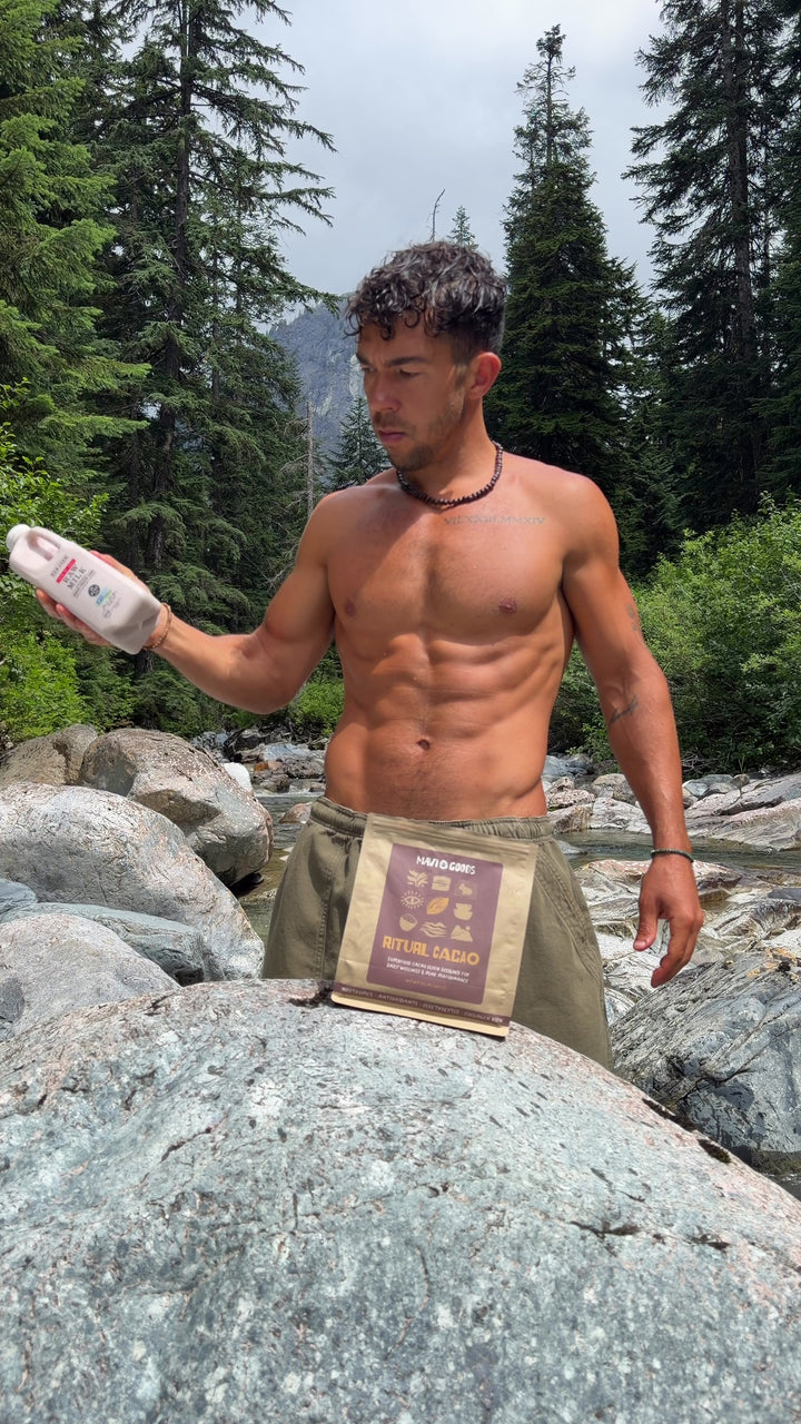 Mavi Goods founder Jason Pabst holding a shaker bottle of Mavi beside a Ritual Cacao bag at a mountain river in Washington